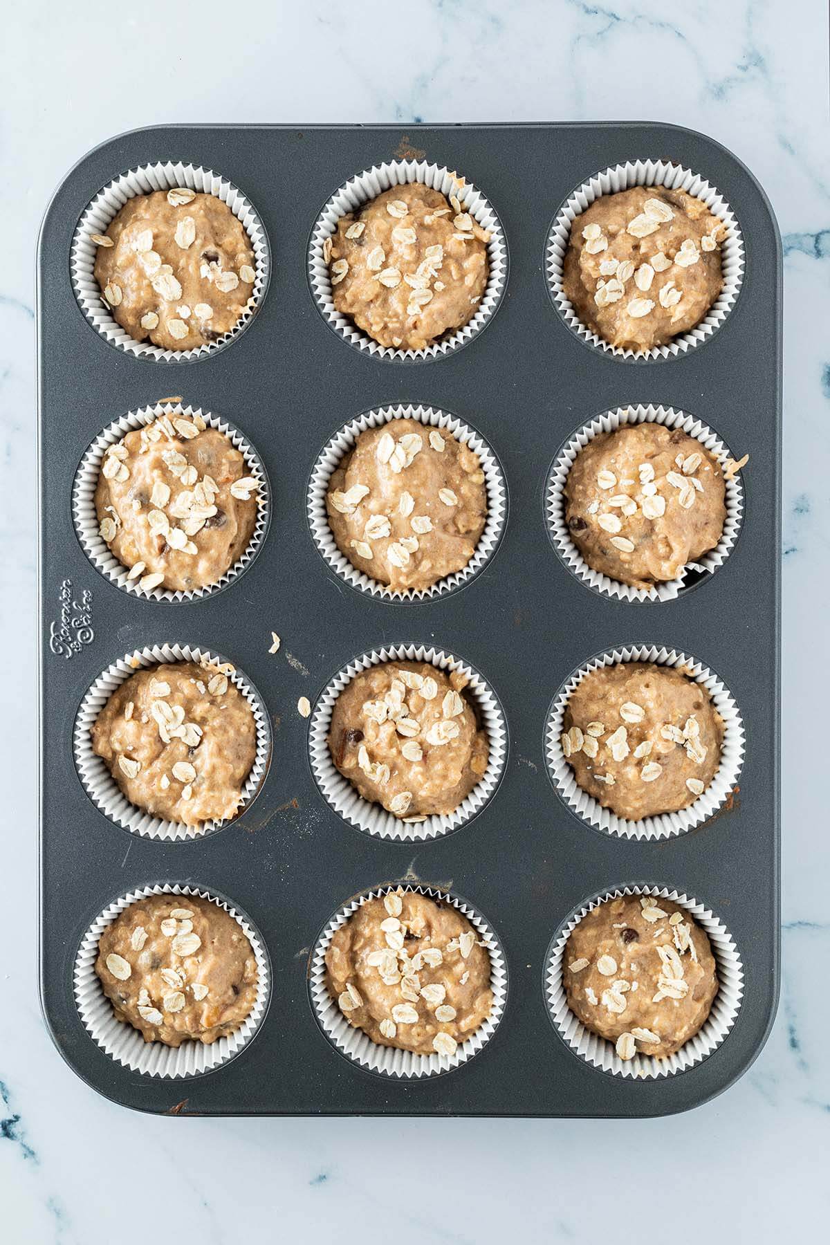 Vogelperspektive auf ein Muffinblech, wo der Teig gleichm&auml;&szlig;ig auf die zw&ouml;lf Vertiefungen aufgeteilt wurde.