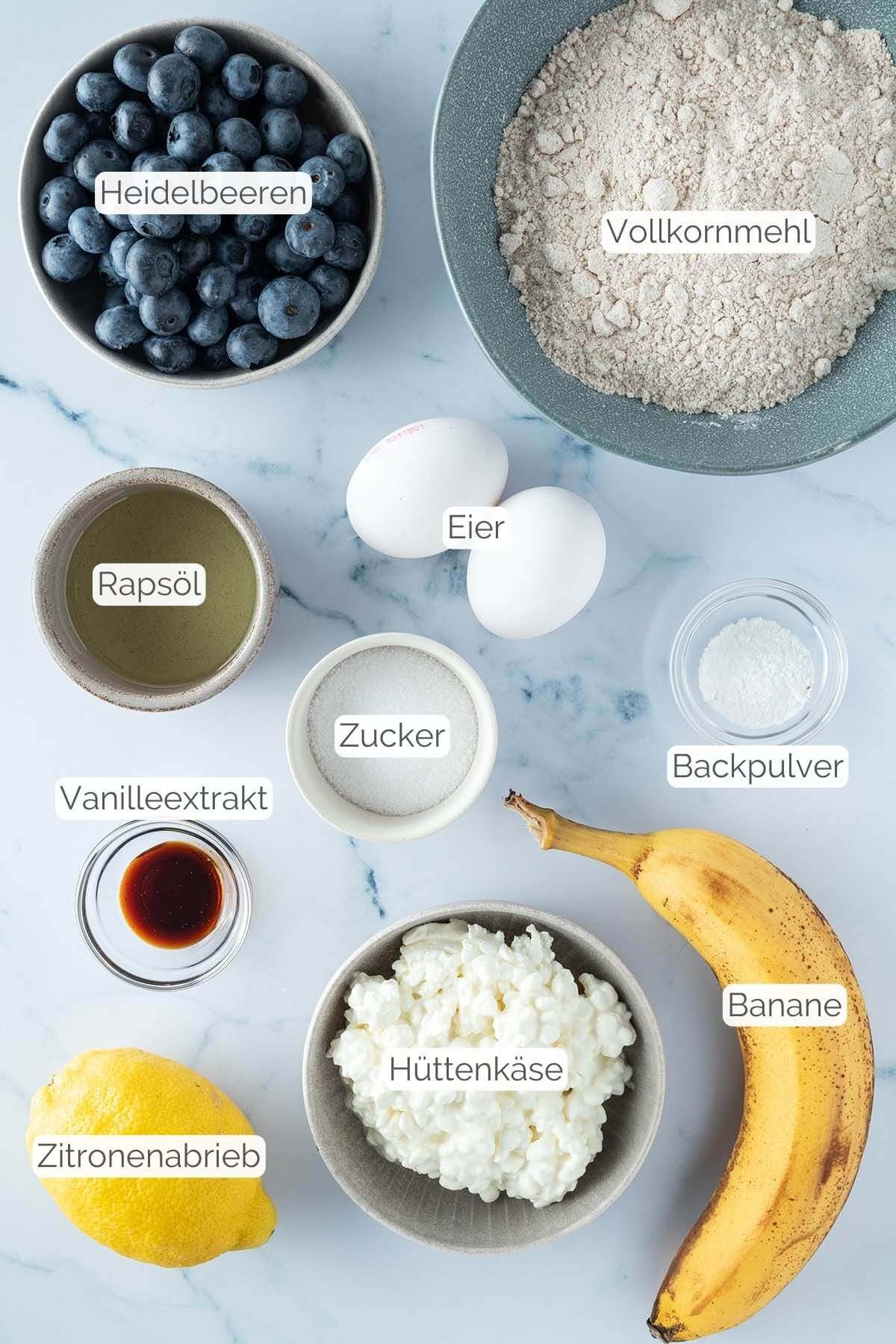 Foto aller Zutaten mit jeweiligen Textbeschriftungen, die f&uuml;r gesunde Blaubeer-Muffins ben&ouml;tigt werden.