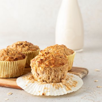 Vier Fr&uuml;hst&uuml;cksmuffins auf einem Brett vor einem beigen Hintergrund mit einer Karaffe Milch.