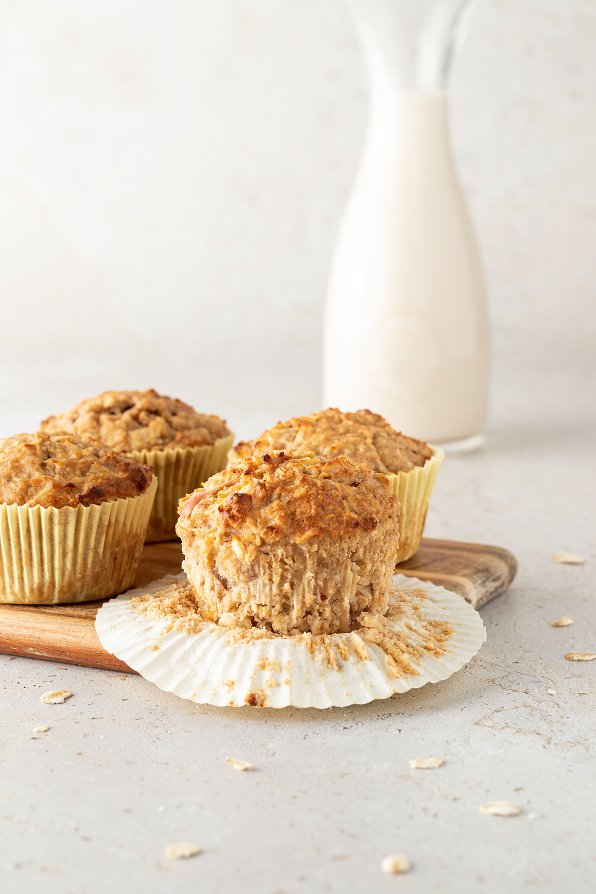 Vier Fr&uuml;hst&uuml;cksmuffins auf einem Brett vor einem beigen Hintergrund mit einer Karaffe Milch.
