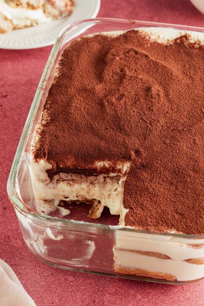 Gesunde Tiramisu ohne Mascarpone in einer Auflaufform auf einem dunkelroten Untergrund.