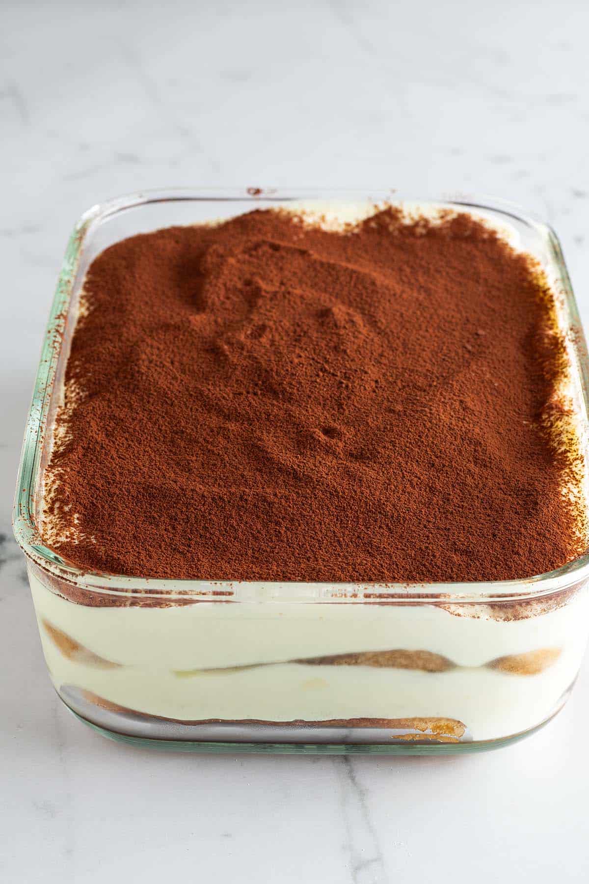 Mit Kakao bestreute Tiramisu ohne Mascarpone und Sahne in einer Glas-Form.