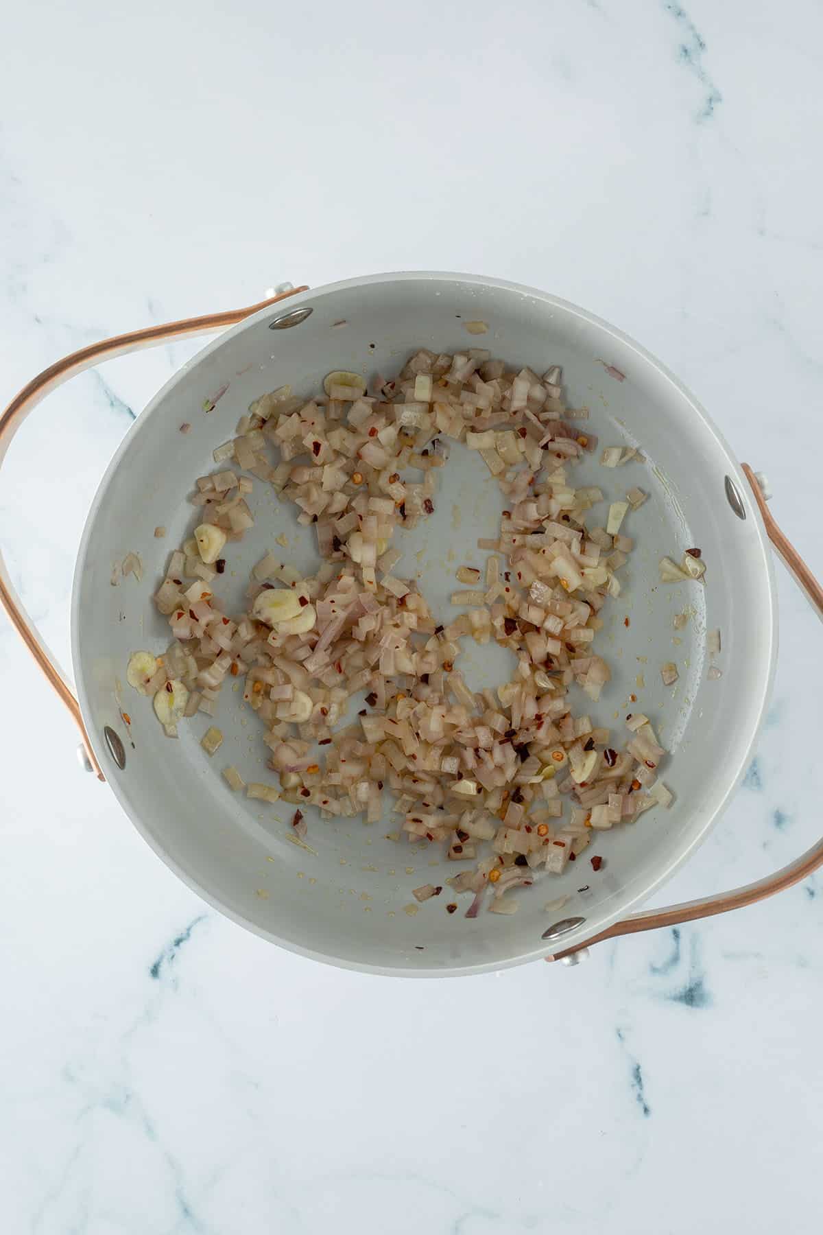Zwiebeln, Knoblauch und Chiliflocken werden in einem Topf angebraten.