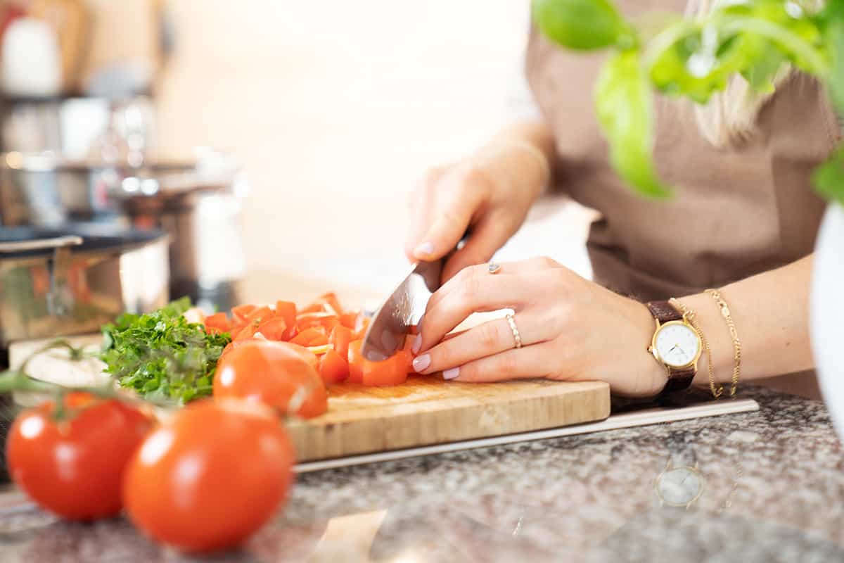 Person schneidet Tomaten auf einem Brett.