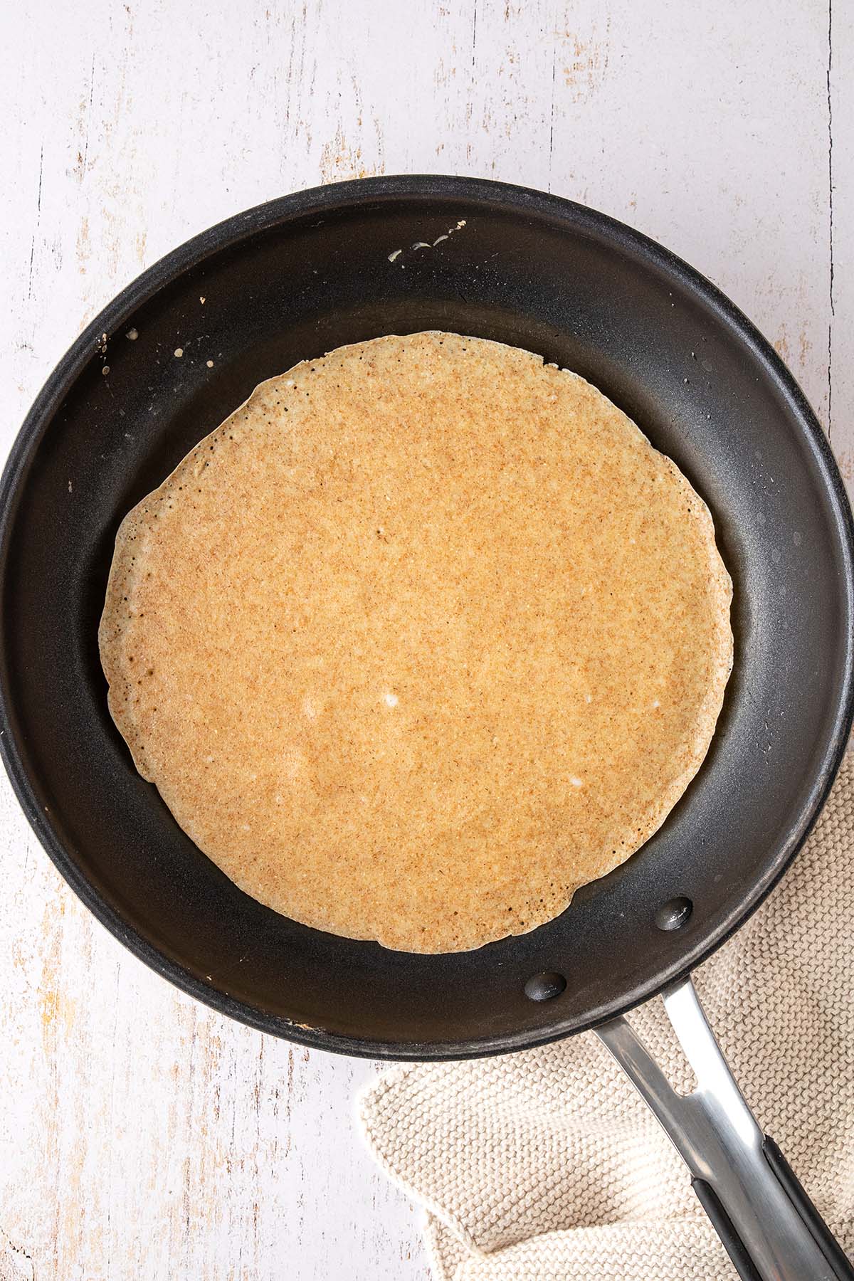 Ein Vollkorn Pfannkuchen mit bereits gestocktem Rand in einer Pfanne.