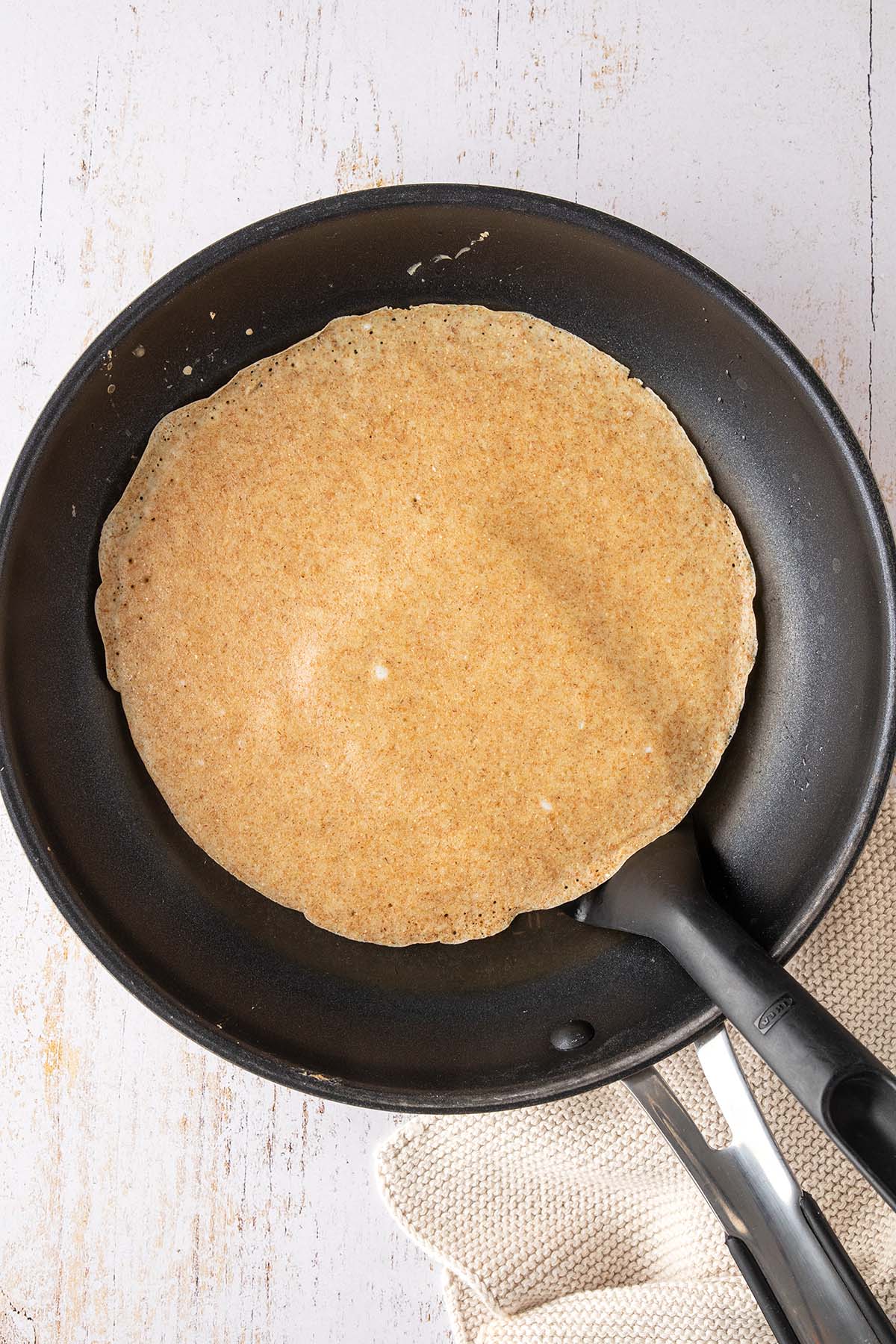 Vogelperspektive auf eine Pfanne, in der ein Pfannkuchen gewendet wird.