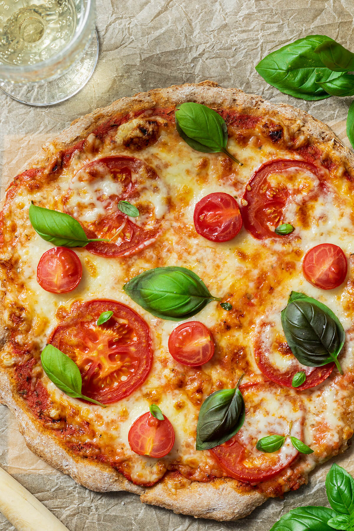 Gesunde Pizza Margarita mit einem Vollkorn Pizzateig auf einem Backpapier mit einem Glas Wein daneben.