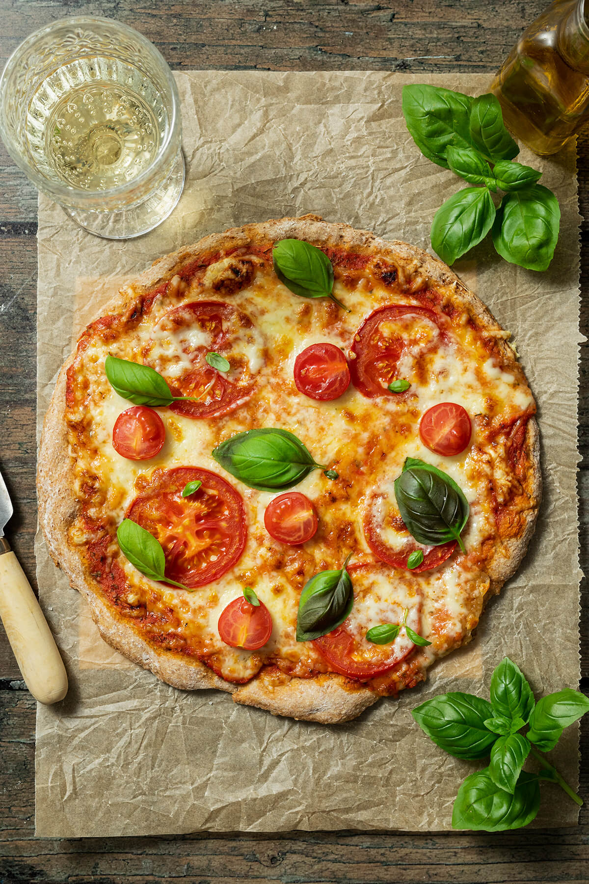 Gesunde Pizza Margarita mit einem Vollkorn Pizzateig auf einem Backpapier mit einem Glas Wein daneben.