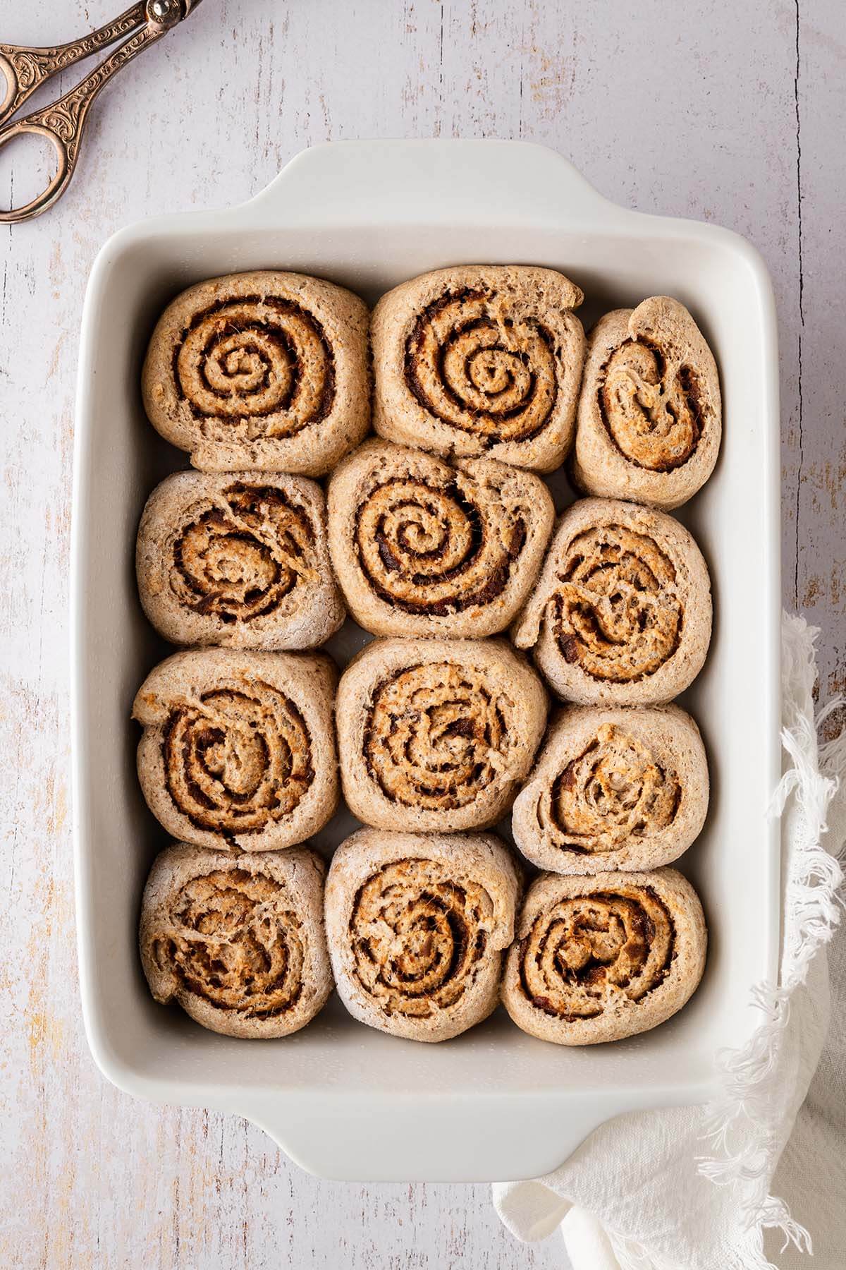 Zw&ouml;lf Vollkorn Zimtschnecken in einer wei&szlig;en Auflaufform.