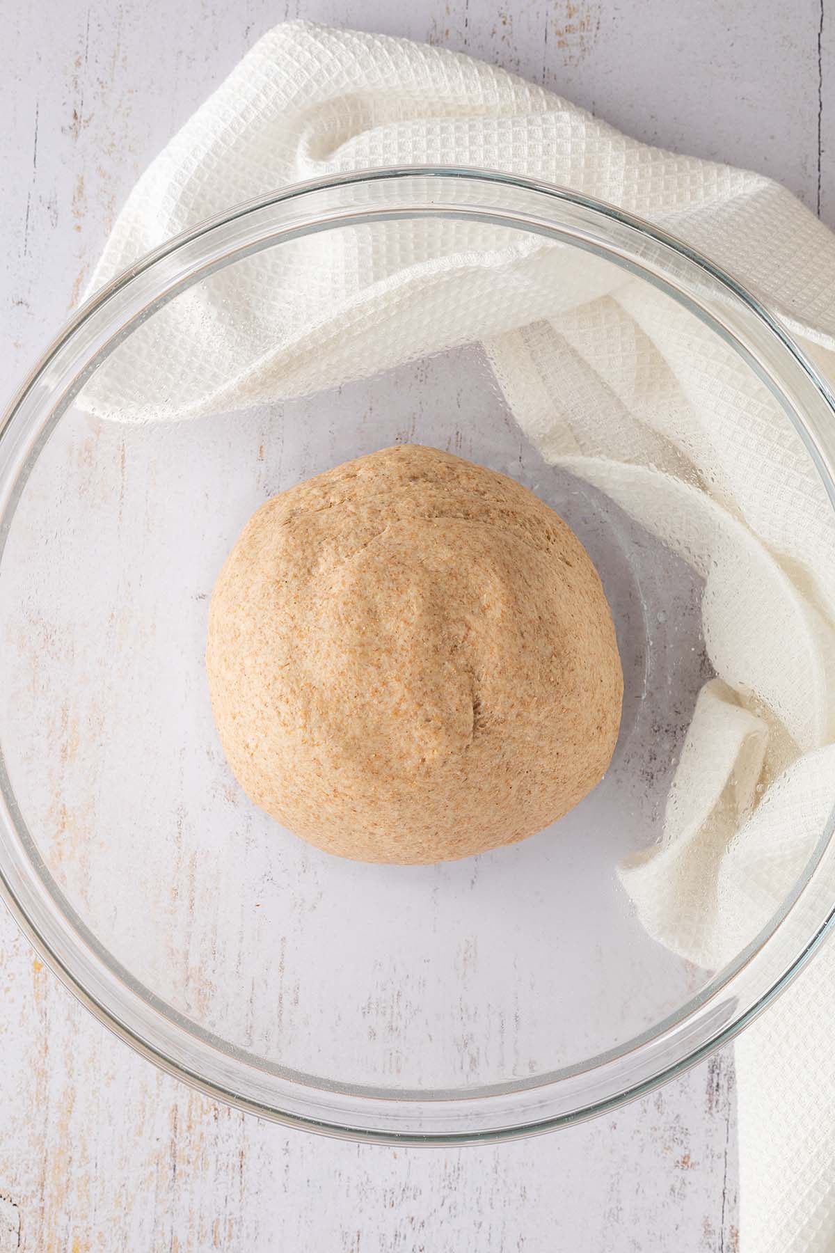 Ein zu einem Ball verkneteter Hefeteig in einer gro&szlig;en Glassch&uuml;ssel.