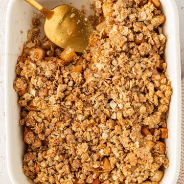 Vogelperspektive auf eine Auflaufform mit einem Apfel Crumble, aus dem bereits eine kleine Portion rausgenommen wurde.
