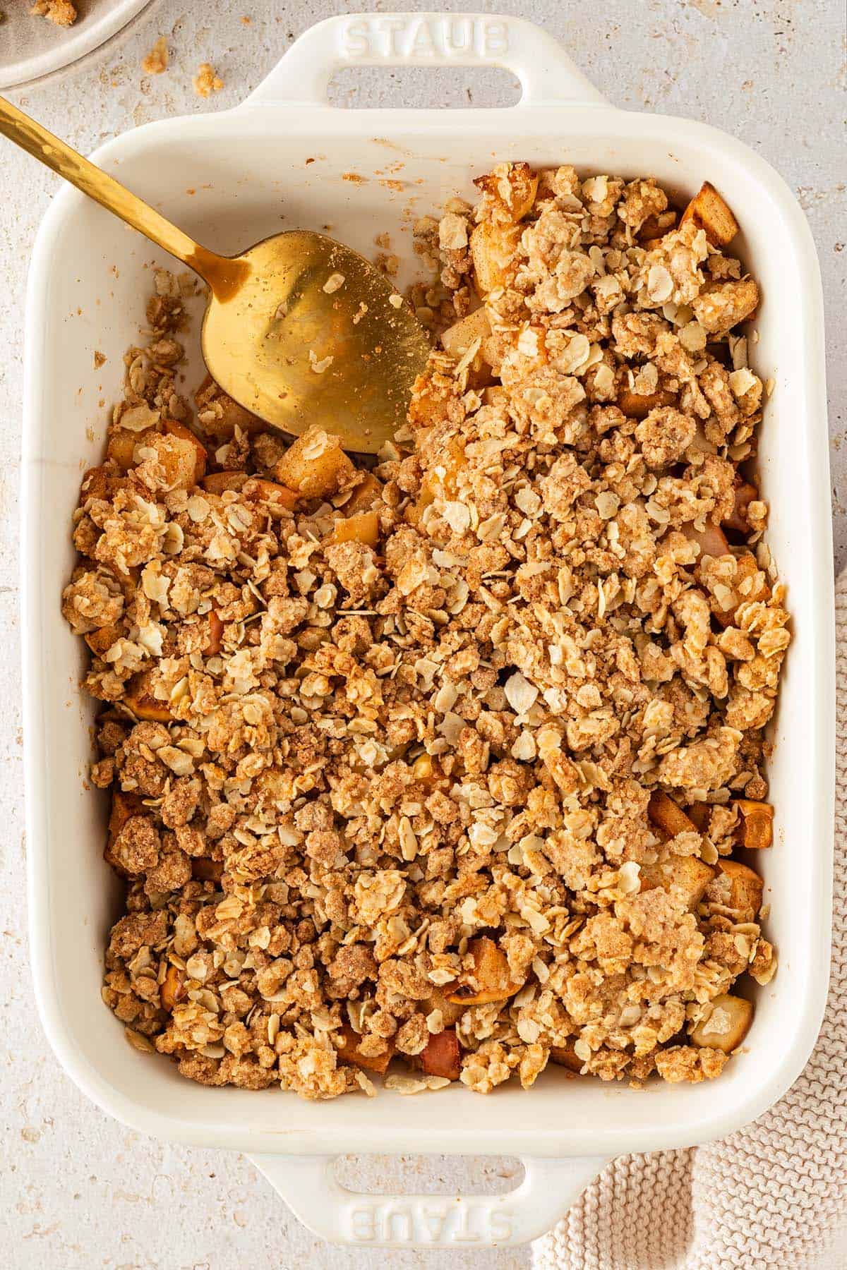 Vogelperspektive auf eine Auflaufform mit einem Apfel Crumble, aus dem bereits eine kleine Portion rausgenommen wurde.