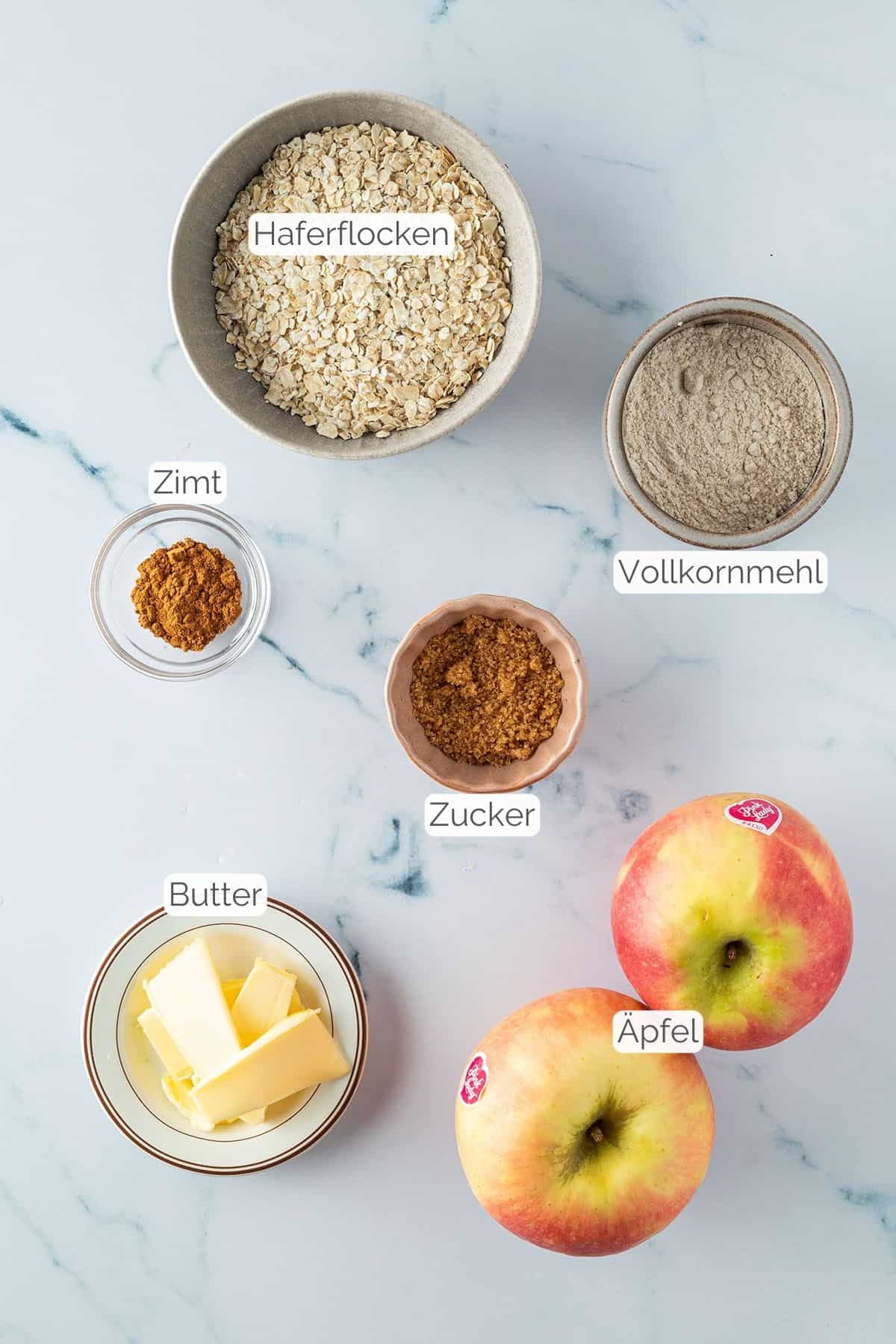 Foto aller Zutaten mit jeweiligen Textbeschriftungen, die f&uuml;r einen gesunden Apfel Crumble ben&ouml;tigt werden.