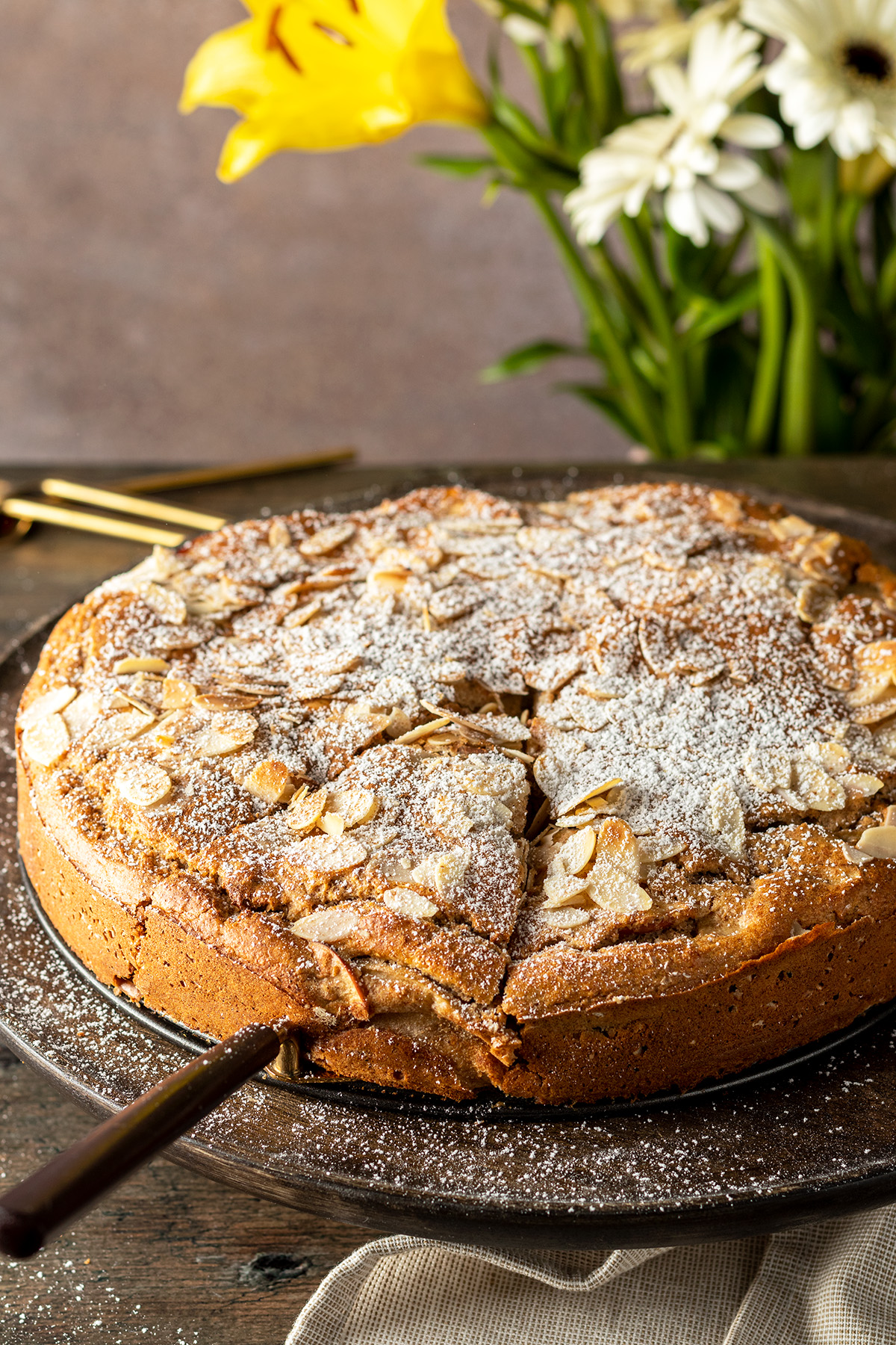 Apfelkuchen mit Mandelbl&auml;ttchen auf der Oberfl&auml;che auf einem Holztisch, im Hintergrund Deko.