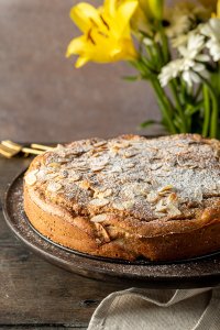 Gesunder Apfelkuchen auf einem Holztisch serviert mit Blumen im Hintergrund.