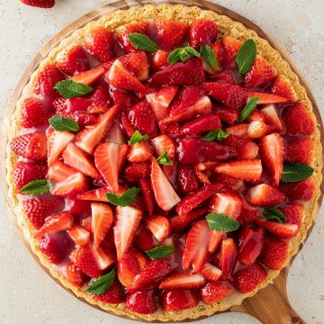 Gesunder Erdbeerkuchen mit frischen Erdbeeren und Minze auf einem runden Holzbrett, das auf einem steinernen Untergrund steht.