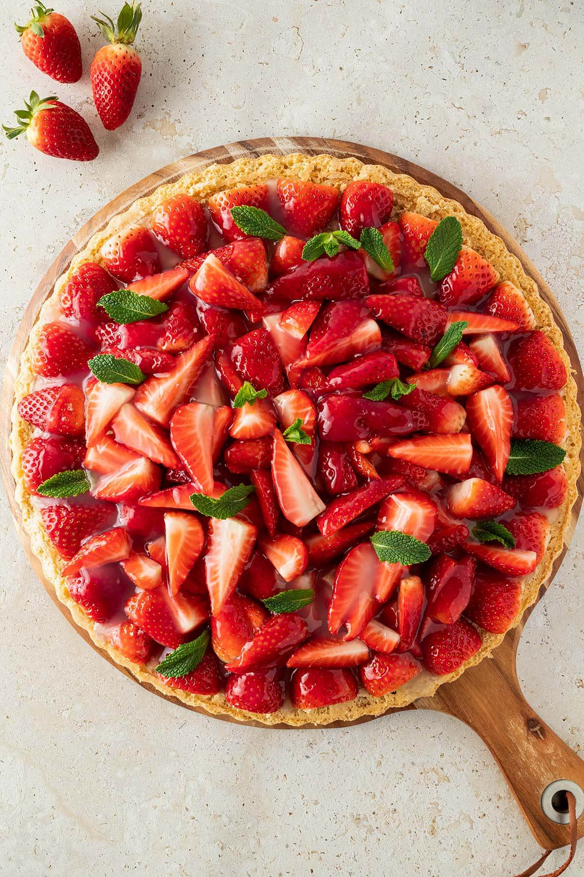 Gesunder Erdbeerkuchen mit frischen Erdbeeren und Minze auf einem runden Holzbrett, das auf einem steinernen Untergrund steht.