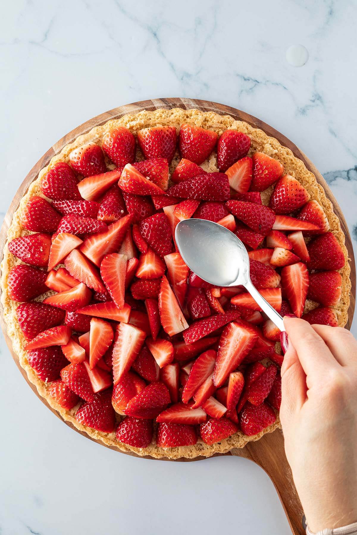 Tortenguss wird mit einem Essl&ouml;ffel &uuml;ber den Erdbeerkuchen verteilt.