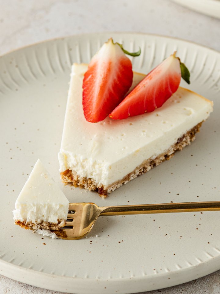 Ein St&uuml;ck K&auml;sekuchen auf einem beigen Teller mit frischen Erdbeeren und einer Kuchengabel.