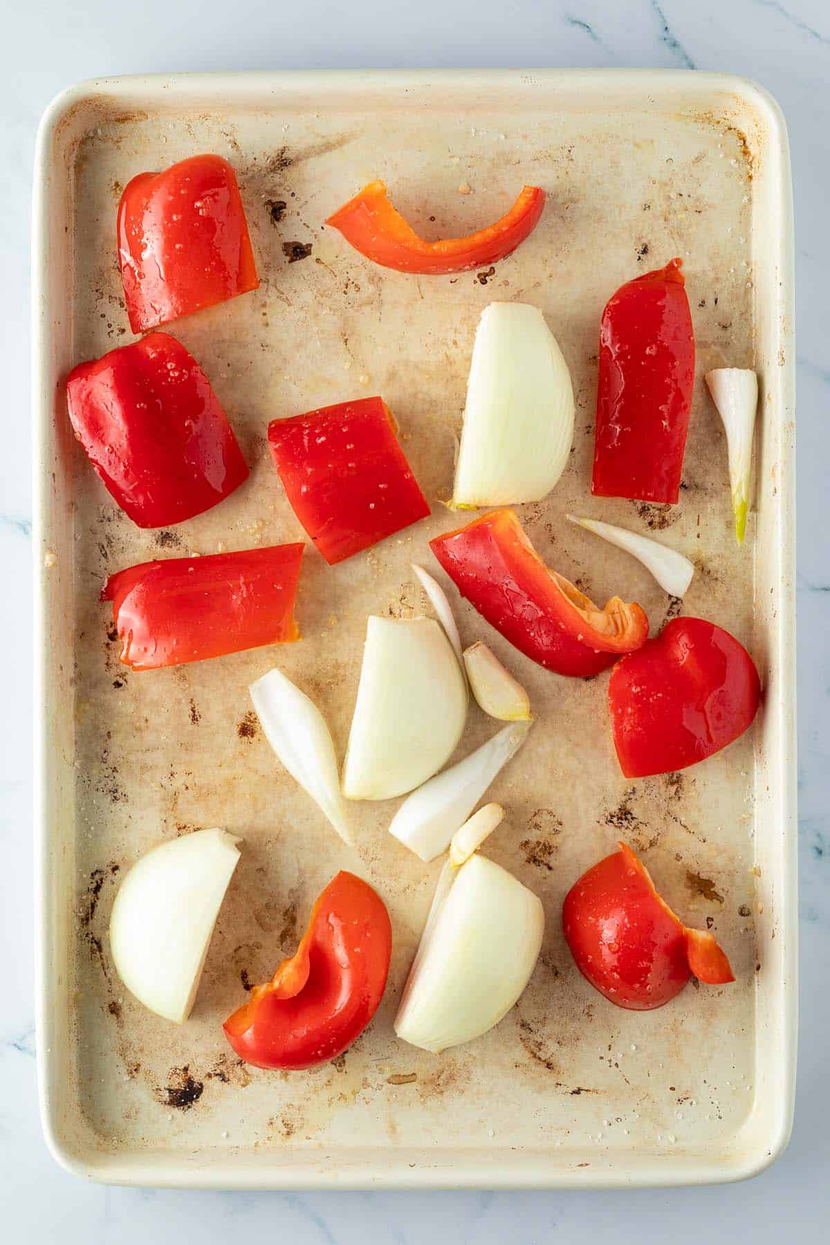 In grobe Stücke geschnittene Paprika, Zwiebeln und Knoblauch auf einem Blech.