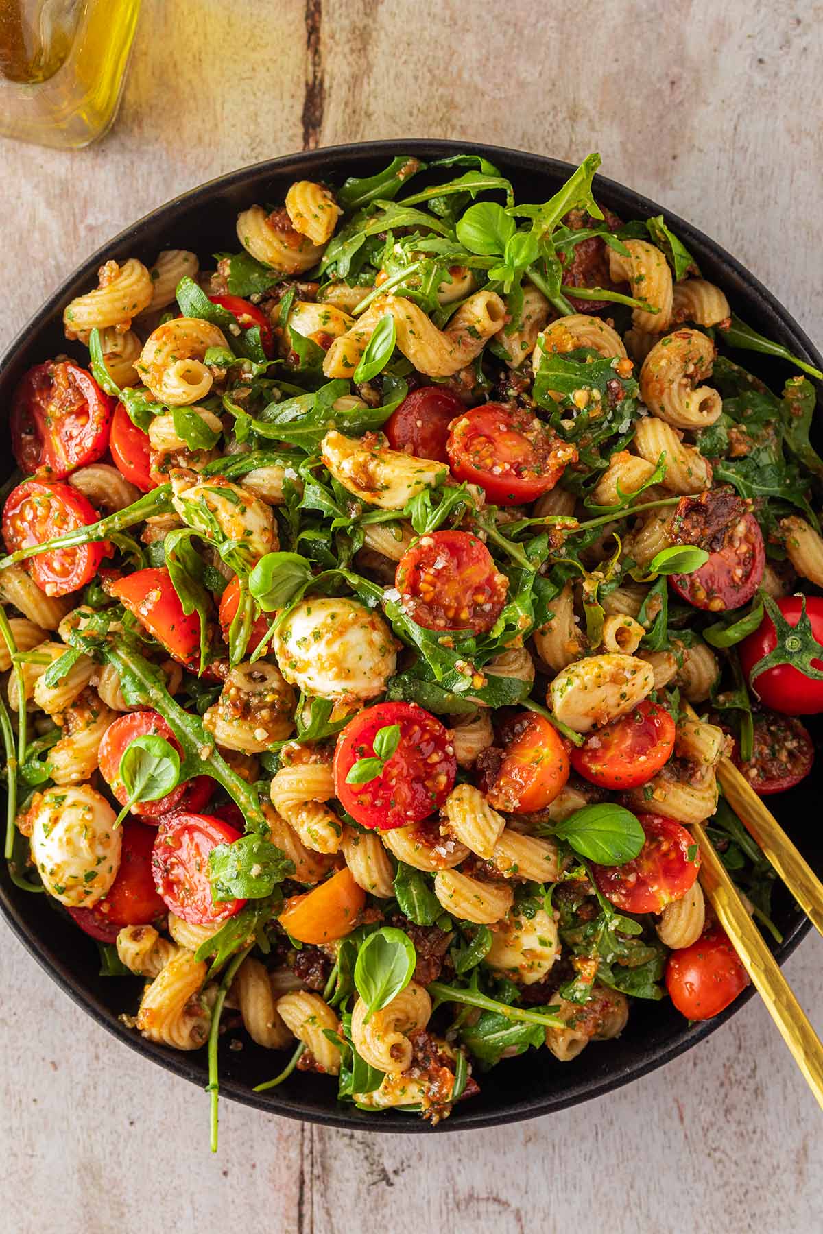 Gro&szlig;e Portion Nudelsalat mit Tomaten, Rucola, Mozzarella und Pesto in einem tiefen Teller.