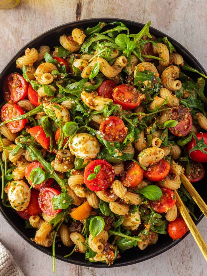 Ein gro&szlig;er Teller mit Nudelsalat mit Tomaten, Rucola, Mozzarella und Pesto.