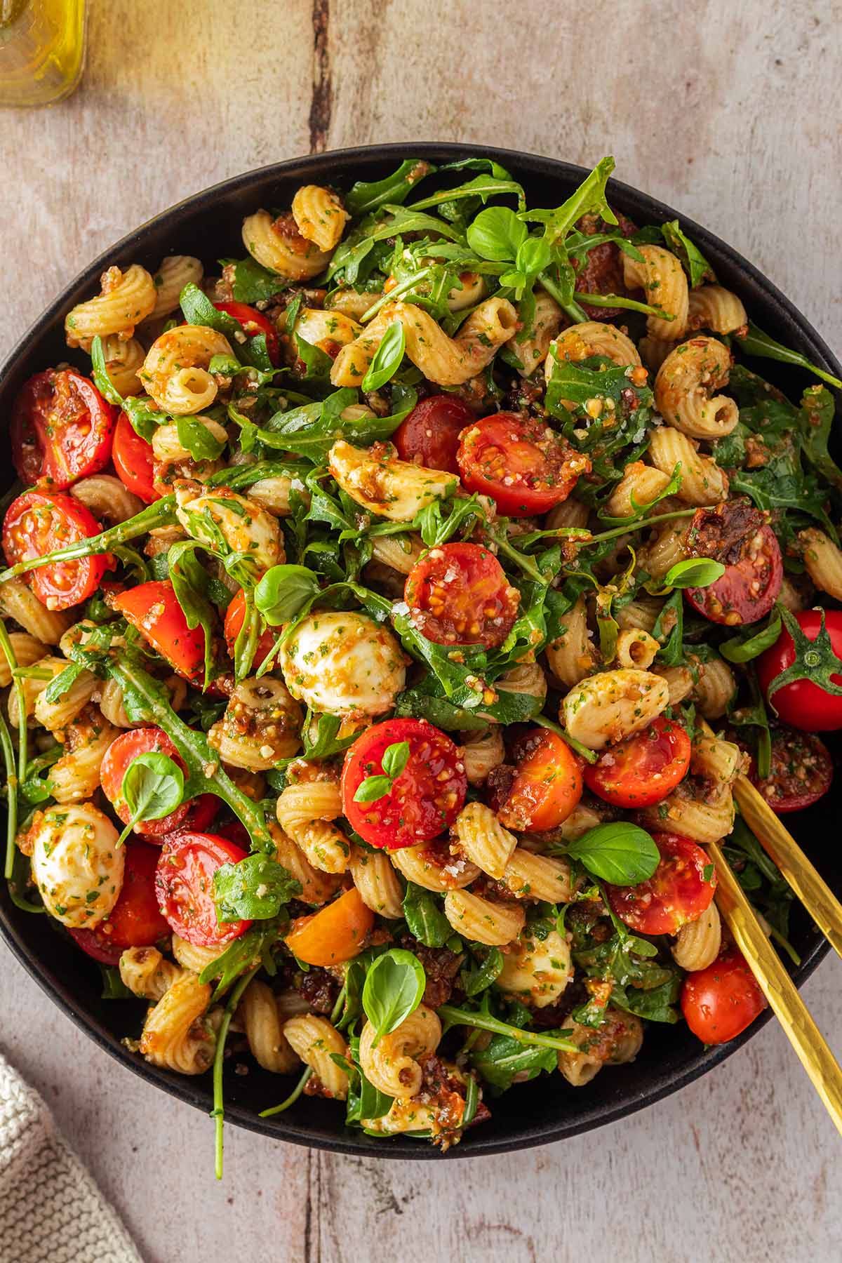 Ein gro&szlig;er Teller mit Nudelsalat mit Tomaten, Rucola, Mozzarella und Pesto.