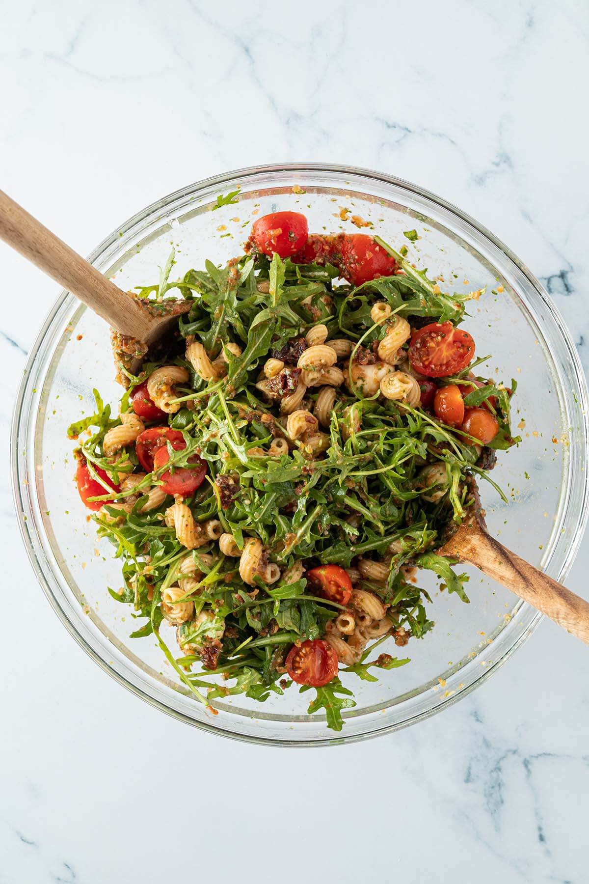 Mediterraner Nudelsalat in einer Glasschüssel mit Salatbesteck.