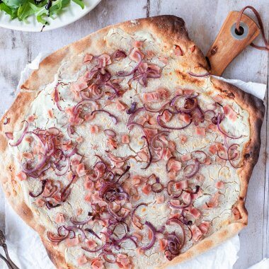 Gesunder Vollkorn Flammkuchen mit Schinken W&uuml;rfel und roten Zwiebeln, serviert mit Salat.