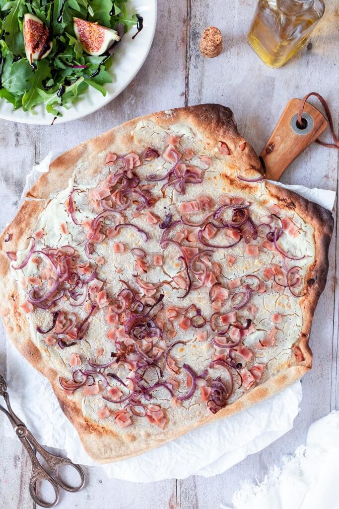 Gesunder Vollkorn Flammkuchen mit Schinken W&uuml;rfel und roten Zwiebeln, serviert mit Salat.