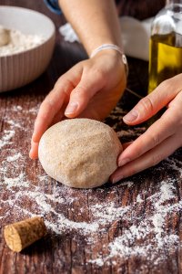 Gesunder Vollkorn Flammkuchenteig ohne Hefe wird auf einer bemehlten Arbeitsfl&auml;che zu einer Kugel geformt.