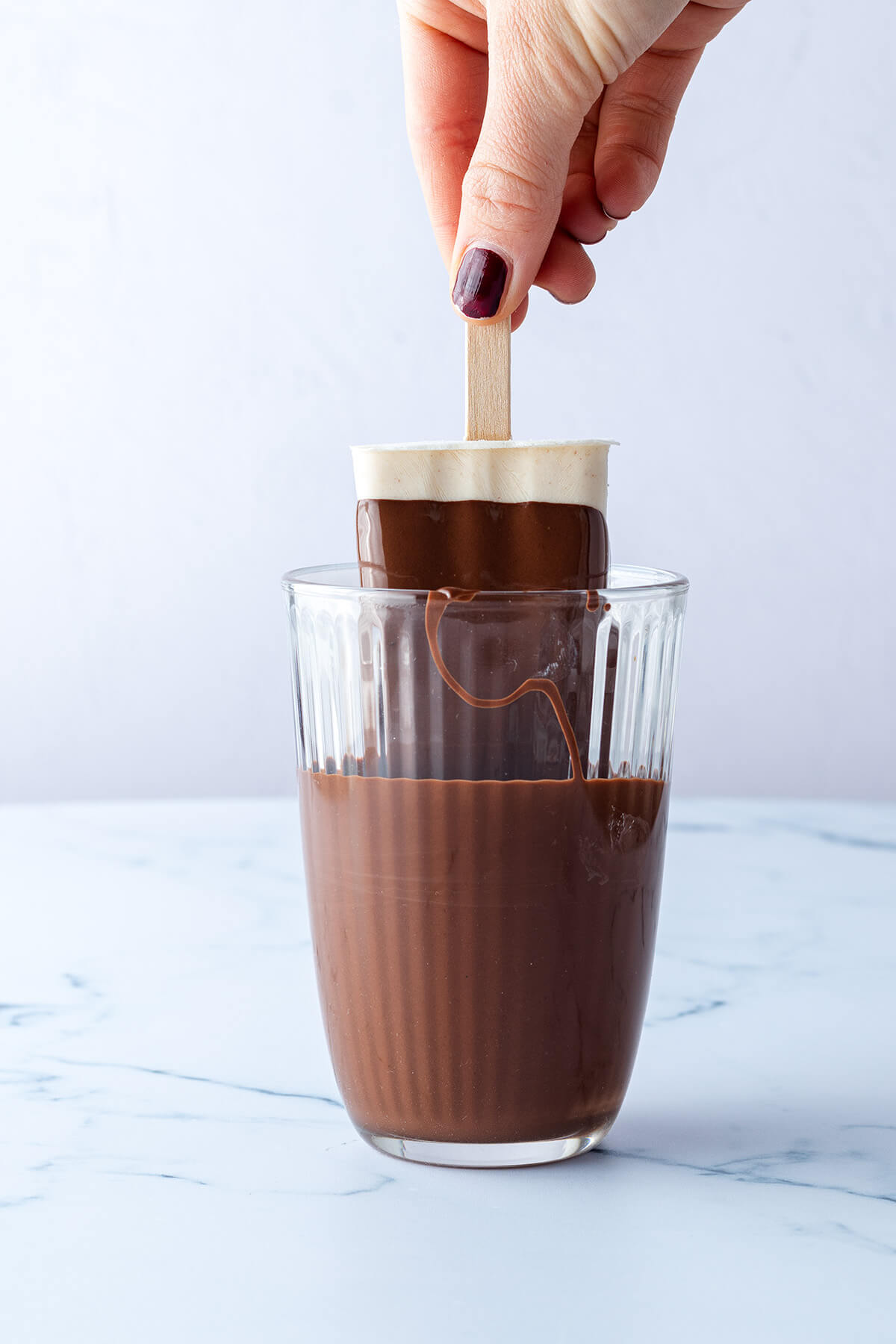 Eis am Stiel wir in ein Glas mit fl&uuml;ssiger Schokolade getaucht.