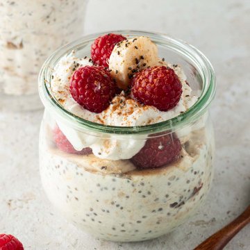 Ein gesundes Fr&uuml;hst&uuml;ck im Glas mit frischen Himbeeren und Bananenscheiben dekoriert auf einem beigen Untergrund. Im Hintergrund ein zweites Glas.