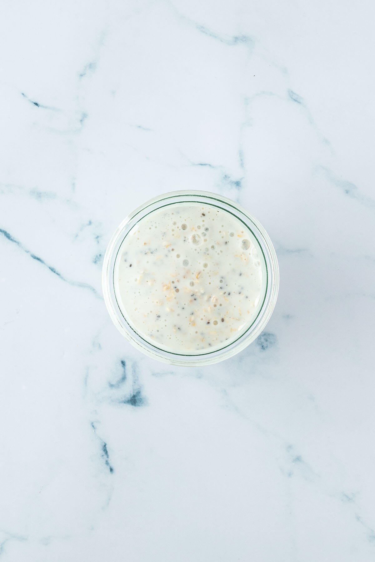 Vogelperspektive auf ein Glas, in dem Haferflocken und Chia Samen mit Milch anger&uuml;hrt wurden.