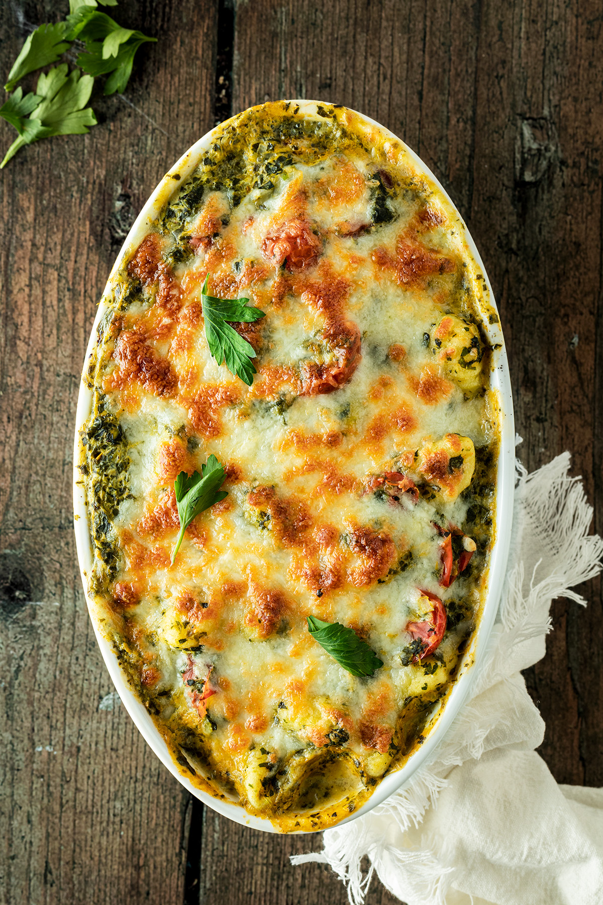Gnocchi Spinat Auflauf mit Mozzarella &uuml;berbacken auf einem braunem Holzhintergrund.