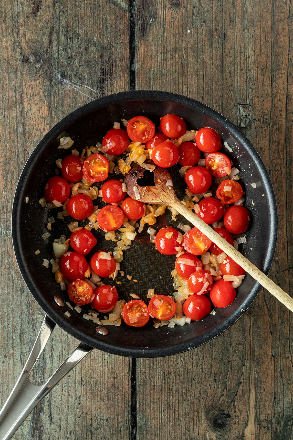 Zwiebel-, Knoblauchw&uuml;rfel und halbierte Cherry Tomaten in einer Pfanne.