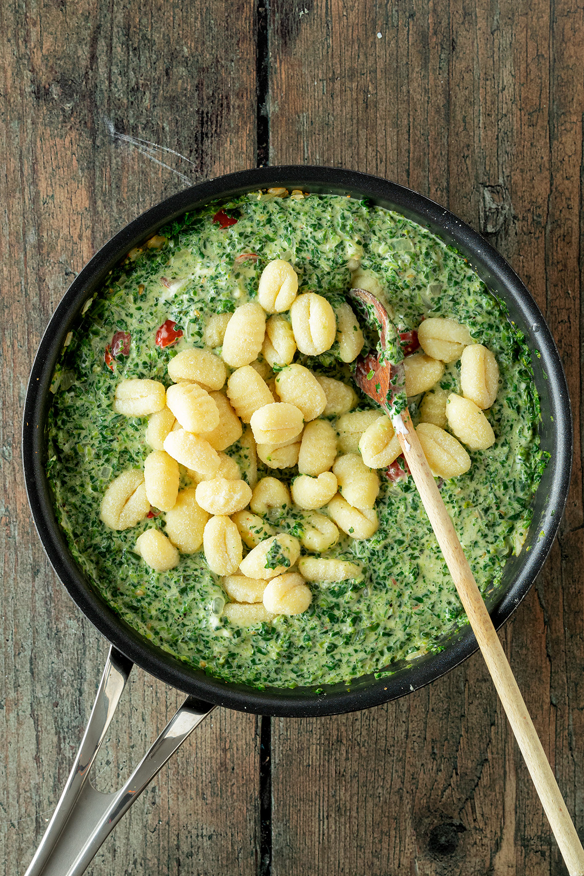 Gnocchi werden in eine cremige Spinatsauce in einer Pfanne gemischt.