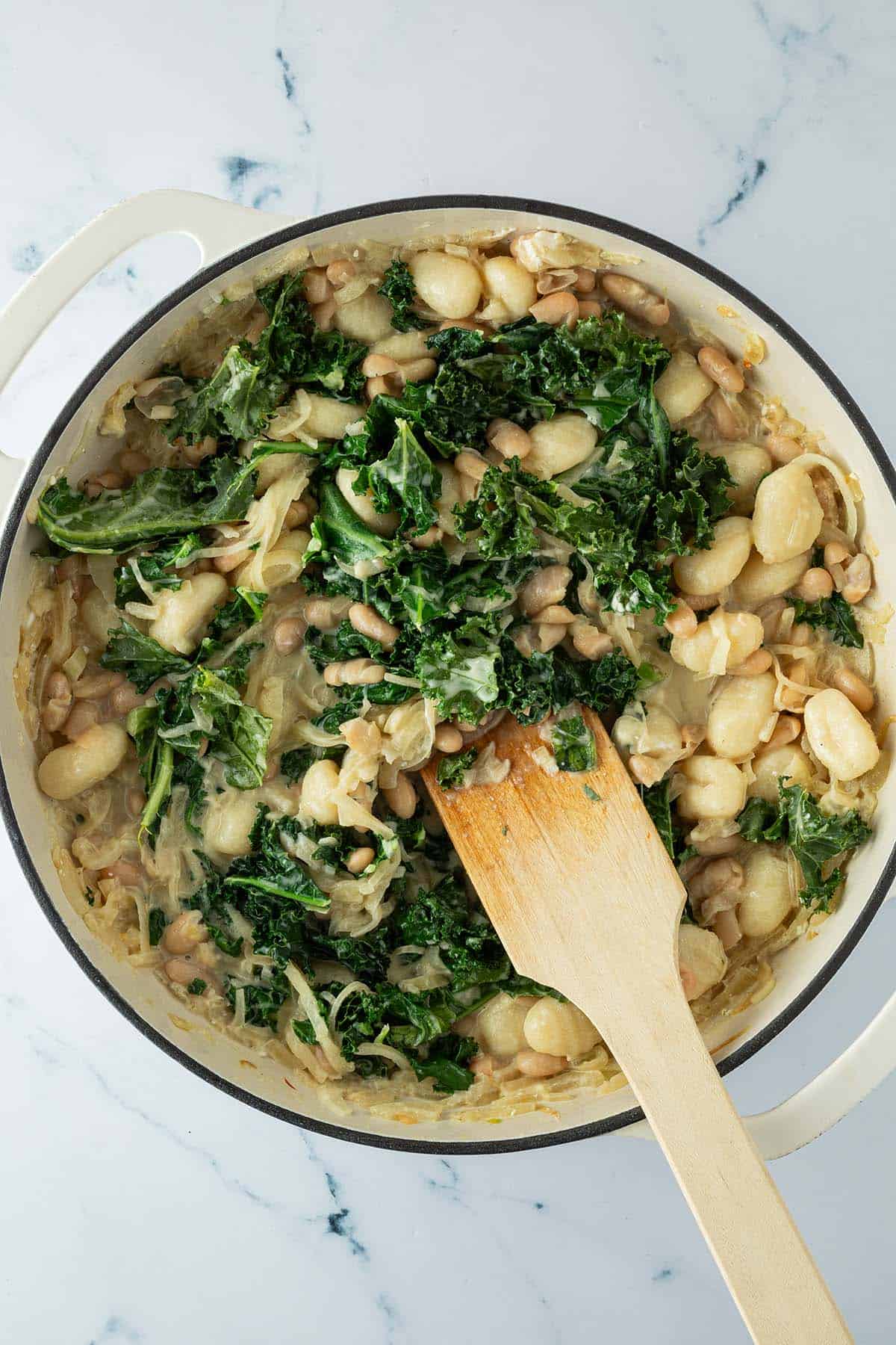 Bohnen, Gnocchi und Grünkohl werden unter die Frischkäse Zwiebelsauce gerührt.