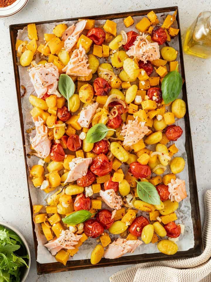 Ein Blech mit im Ofen ger&ouml;steten Gnocchi, K&uuml;rbisw&uuml;rfeln, Tomaten und Lachsst&uuml;ckchen.