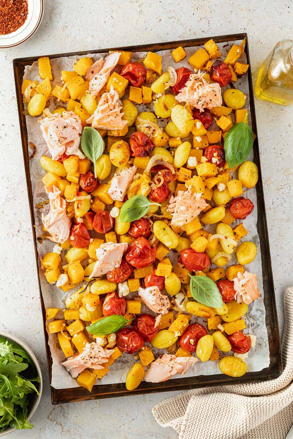 Ein Blech mit im Ofen ger&ouml;steten Gnocchi, K&uuml;rbisw&uuml;rfeln, Tomaten und Lachsst&uuml;ckchen.
