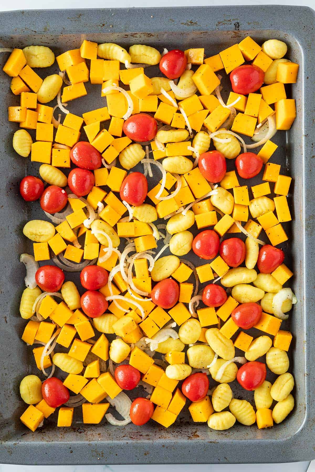 Rohe K&uuml;rbisw&uuml;rfel, Gnocchi, Tomaten und Zwiebelringe auf einem Blech.