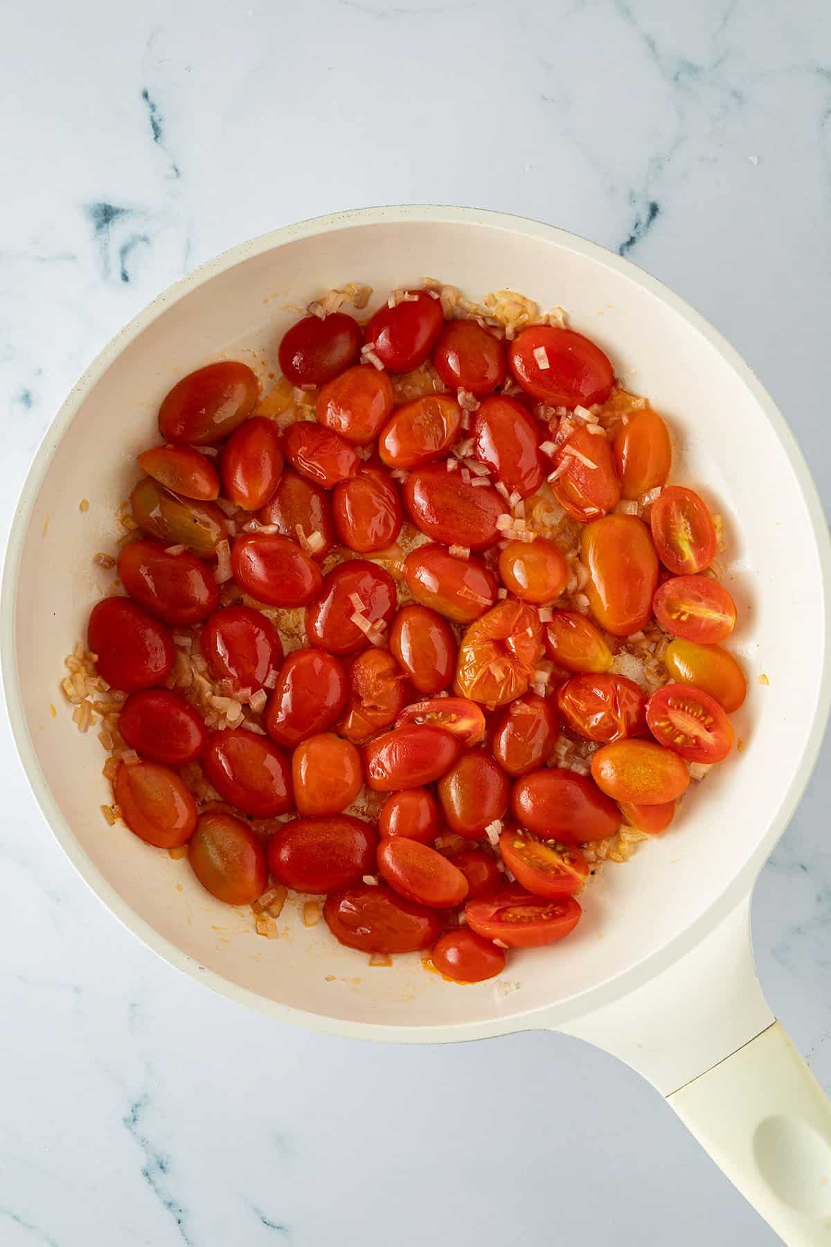 Halbierte Kirschtomaten und fein gew&uuml;rfelte Zwiebeln werden in einer Pfanne angebraten.