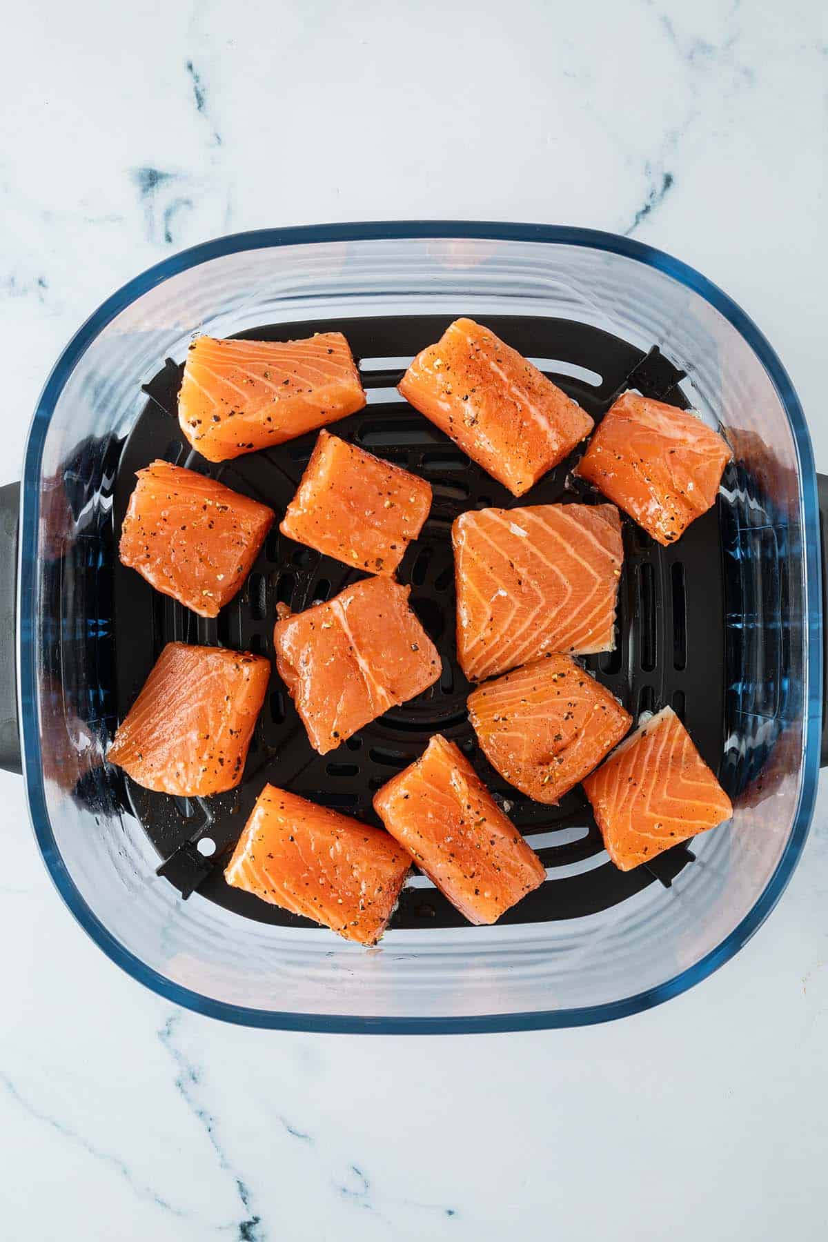 Rohe Lachsw&uuml;rfel, gew&uuml;rzt mit Salz und Pfeffer, gleichm&auml;&szlig;ig im Airfryer-Korb verteilt.