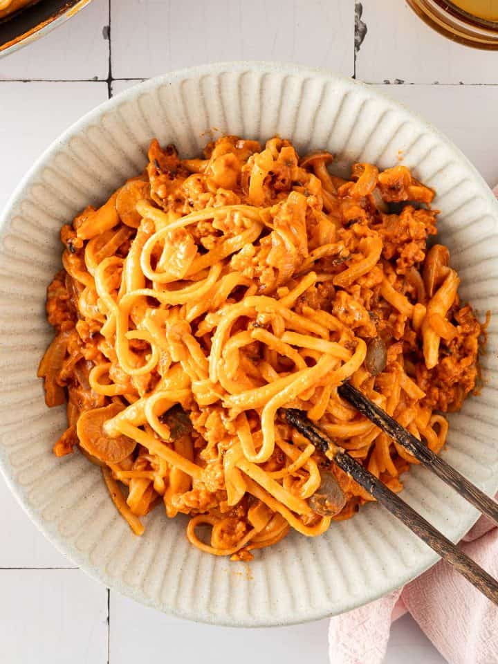 Cremige Gochujang-Nudeln mit gebratenem Tempeh und Pilzen in einer Sch&uuml;ssel, serviert mit Essst&auml;bchen.