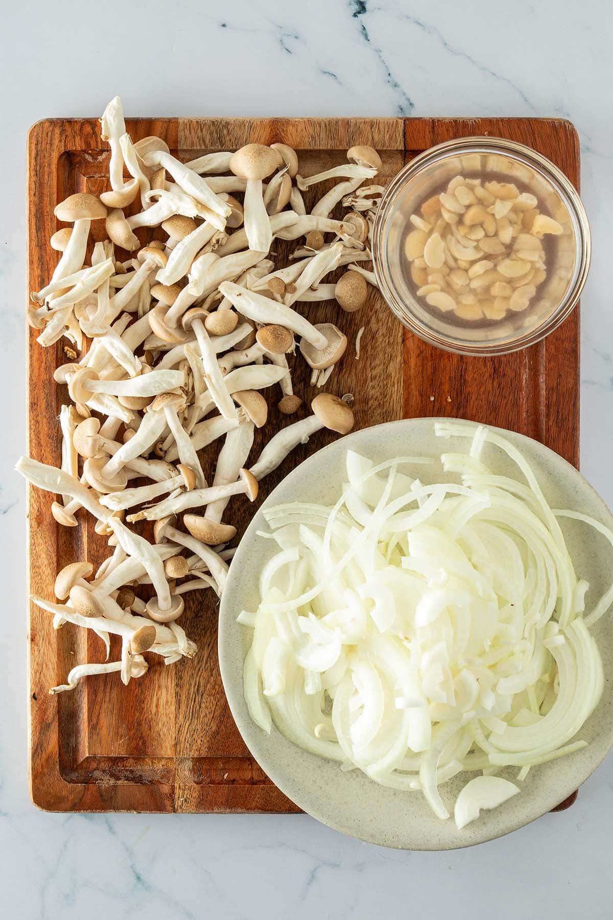 Frische Pilze, geschnittene Zwiebeln und eingeweichte Cashews auf einem Holzbrett vorbereitet.