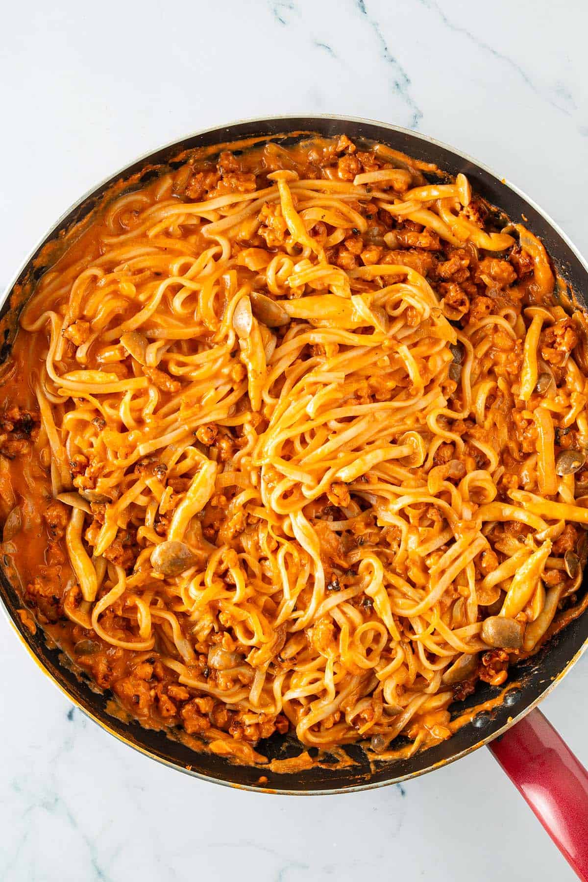 Pfanne mit Nudeln, Pilzen, Zwiebeln und Tempeh in einer cremigen Gochujang Sauce.
