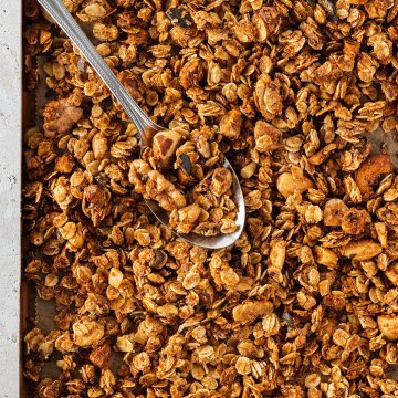 Ein L&ouml;ffel nimmt eine Portion Granola von einem Blech mit knusprigem, goldbraunem Granola.