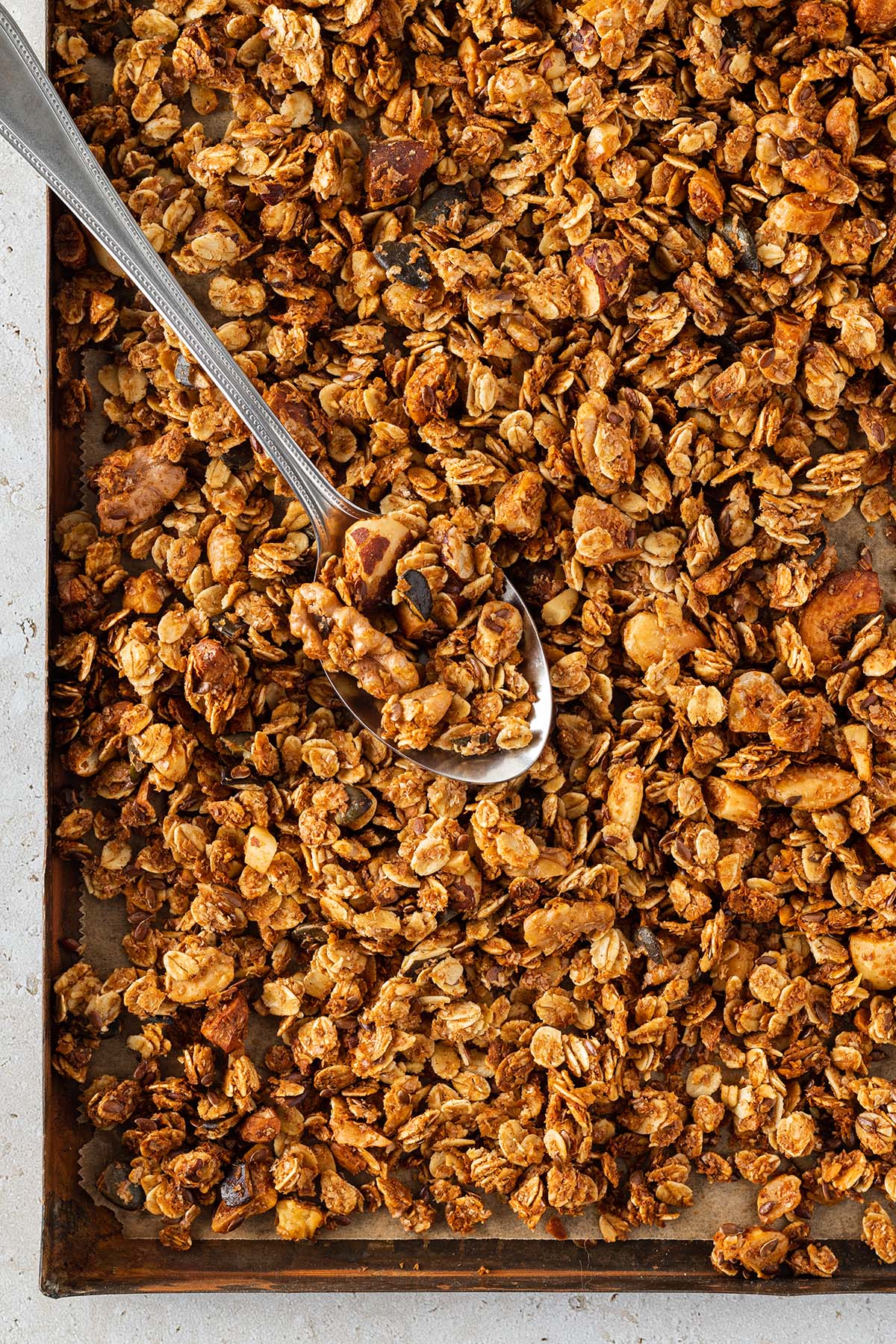 Ein L&ouml;ffel nimmt eine Portion Granola von einem Blech mit knusprigem, goldbraunem Granola.