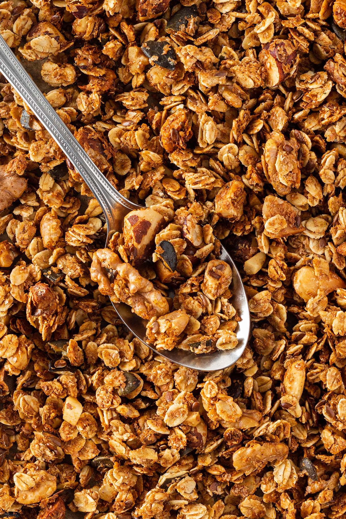 Nahaufnahme von einem knusprigen Granola mit einem silbernen L&ouml;ffel darin.
