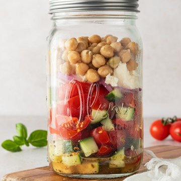 Griechischer Salat mit Kichererbsen in einem gro&szlig;en Schraubglas vor beigen Hintergrund, Deko im Bildrand.